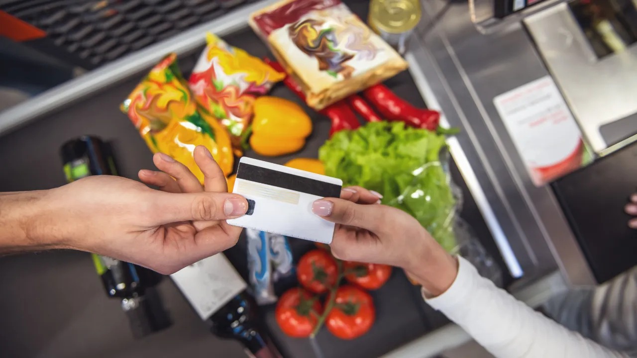 An_overhead_shot_of_a_grocery_shopper_handing_a_credit_card_to_a_cashier_at_checkout_11zon